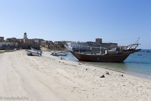 der Strand mit einem Fischerboot vor dem Fort von Mirbat im Oman