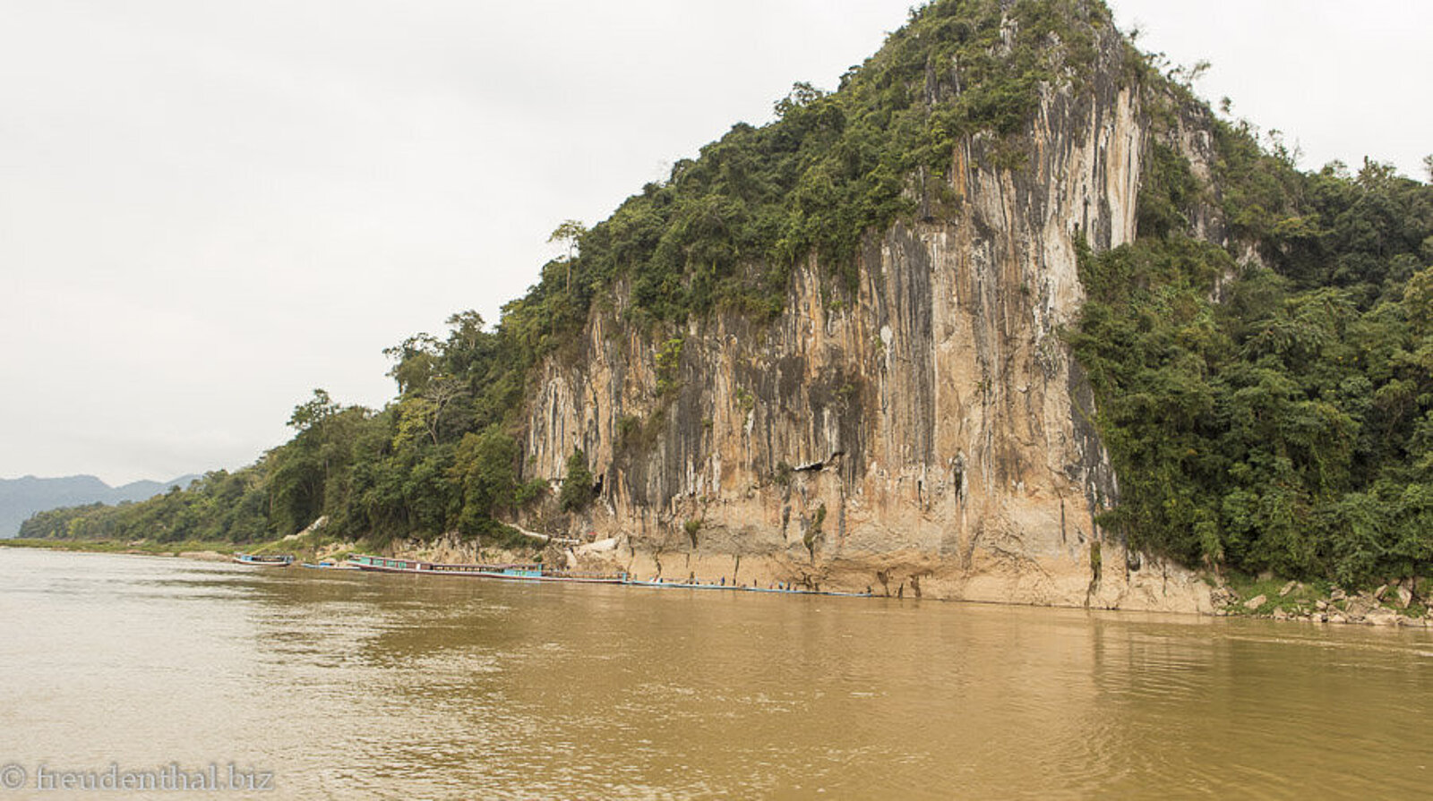 Blick über braunes Wasser im Mekong zu den Pak-Ou-Höhlen Tham Ting in Laos