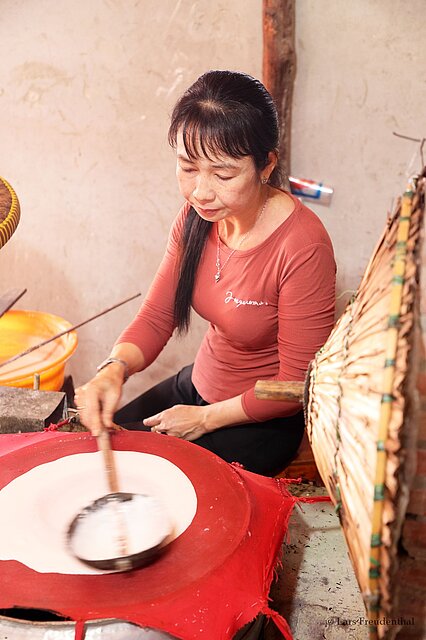 eine Vietnamesen verteilt den Teig für die Herstellung von Reispapier auf einem gespannten Tuch