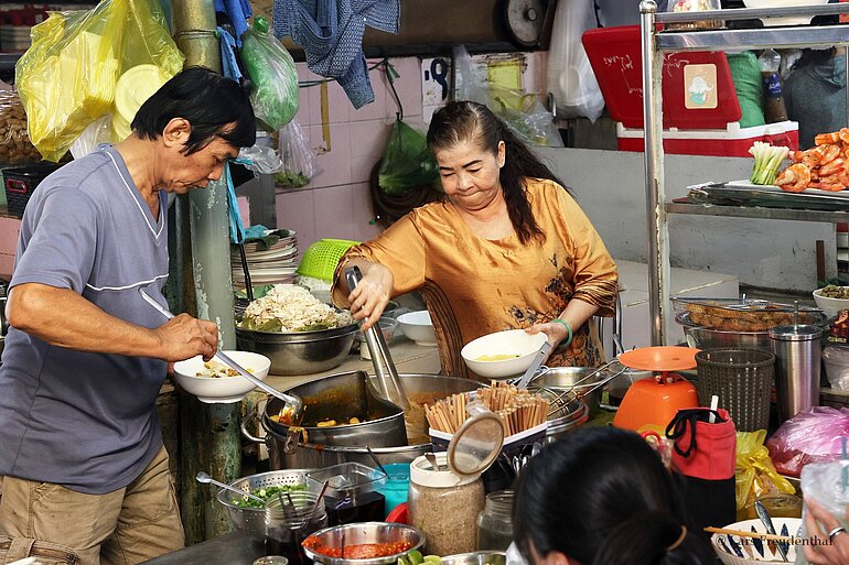 Eine Frau gibt Essen bei einer Garküche im Ben-Thanh-Markt aus.